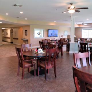 A spacious dining area with multiple tables and chairs, featuring a ceiling fan and a television on the wall.