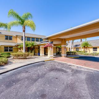 The image shows the exterior of a hotel with a covered entrance and surrounding palm trees.
