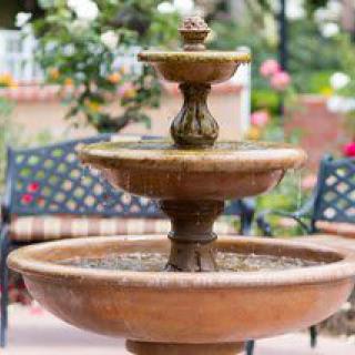 A tiered garden fountain with a bench in the background.
