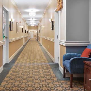 A spacious, well-lit hallway with patterned carpet and a blue chair on the side.