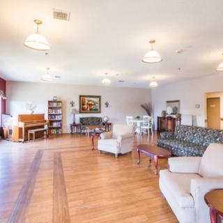 A spacious and well-furnished living room with a piano, sofas, armchairs, and hardwood flooring.