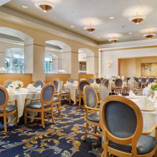An elegant dining room with round tables and upholstered chairs, set for an event.