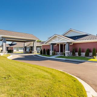 A spacious building with a nicely landscaped lawn and driveway on a sunny day.
