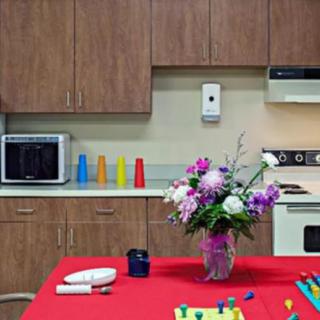 A kitchen with wooden cabinets, a microwave, colorful cups, and a table adorned with a bouquet of flowers.