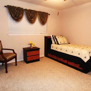 A minimalist bedroom with a single bed, nightstand, and chair, featuring neutral tones and simple decor.