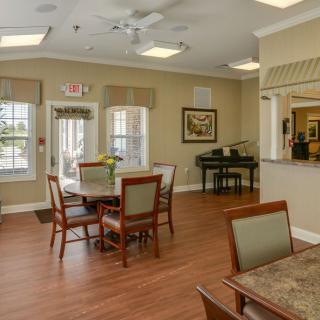A cozy dining area with tables, chairs, and a piano by the window.