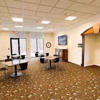 A spacious waiting area with tables, chairs, and a television in a carpeted room.