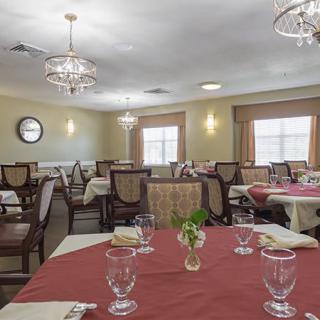 An elegant dining room with several tables and chairs, featuring chandeliers and neatly arranged place settings.