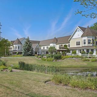 A picturesque residential house with a pond and landscaped surroundings under a clear blue sky.