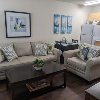A cozy living room with a sofa, armchair, coffee table, and kitchen area.