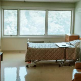 A clean and well-lit hospital room with a single bed and large windows.