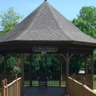 A wooden gazebo in a park surrounded by trees.
