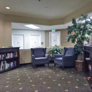 A cozy lobby featuring two armchairs, a bookshelf, and decorative plants.