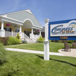 A view of the Compass Insurance office with a sign and well-maintained lawn on a sunny day.