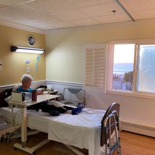 A patient room in a hospital with a bed, a table, and natural light coming through the window.