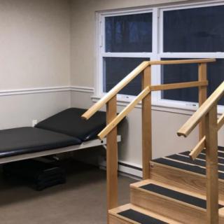 A physical therapy room featuring a set of wooden stairs and a treatment bed.