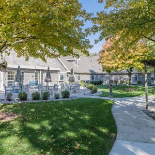 A scenic view of a pathway leading through an outdoor area with autumn trees and a building with patio chairs.