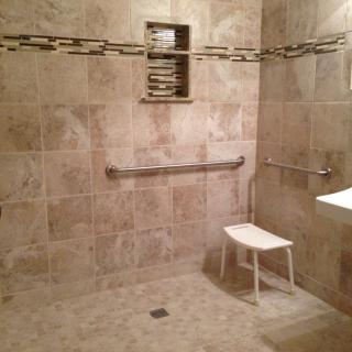 An accessible bathroom with a shower area featuring grab bars and a chair.