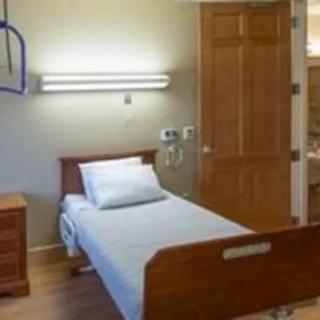 A simple hospital room with a single bed and wooden furnishings.