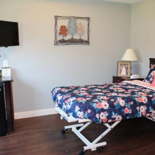 A cozy bedroom featuring a floral patterned bedspread, a bedside lamp, and a wall-mounted television.