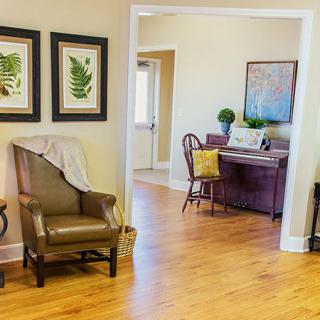 A cozy living room with an armchair, artwork on the walls, and a view into the dining area.