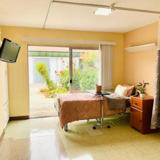 A well-lit hospital room featuring a patient bed with a garden view outside.