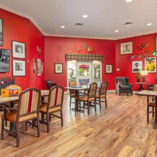 A cozy dining area with red walls, decorated with framed pictures and featuring multiple tables and chairs on a wooden floor.
