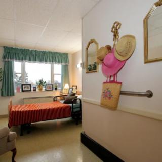A neatly arranged bedroom with wall decorations, a bed covered with a red blanket, and a window with green curtains.
