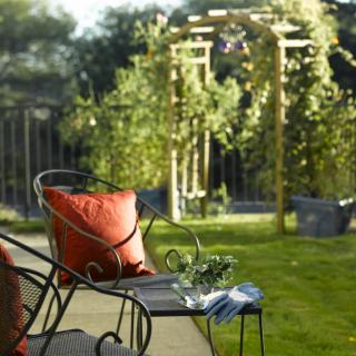 A tranquil garden setup with a cozy chair and a view of an archway surrounded by lush greenery.