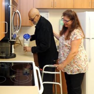 An elderly person receiving assistance from a caregiver in the kitchen.