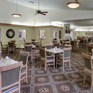 An empty dining room with neatly arranged tables and chairs, featuring a decorative carpet and overhead lighting.