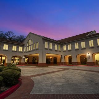 A well-lit building with arched entrances and manicured landscaping during the evening.