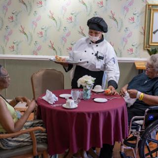 A chef serves refreshments to residents in a cozy dining area of a nursing home.