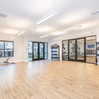 A spacious and modern yoga studio with bright lighting, wooden floors, and large windows.