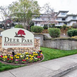 Entrance sign of Deer Park Retirement Community surrounded by landscaping and flowers.