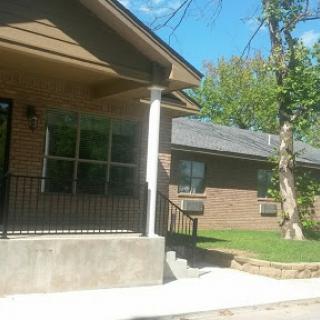 A view of a residential house with a porch and trees nearby.