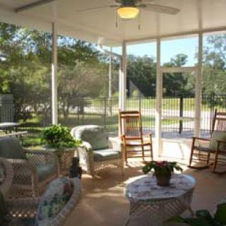 A cozy sunroom with wicker furniture, rocking chairs, and indoor plants, bathed in natural light.