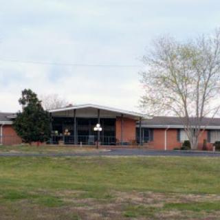 A view of a single-story brick building surrounded by grass and trees.