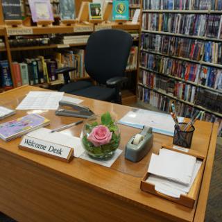 A neatly organized desk in a library, featuring stationery and a decorative flower arrangement.