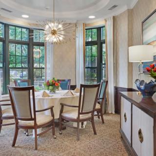 A well-lit dining room featuring a round table with chairs, a modern chandelier, and large windows.