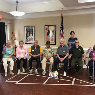 A group of seniors seated together for a community event indoors, with the USA flag in the background.