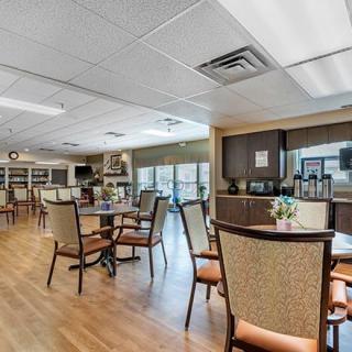 A spacious dining area with tables and chairs, featuring a wooden floor and large windows for natural light.