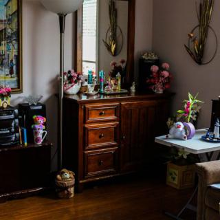 A cozy living room corner with a wooden dresser, decorative flowers, and a standing lamp.