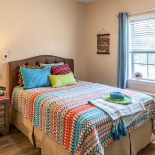 A cozy and colorful bedroom featuring a neatly made bed with vibrant throw pillows and a decorative blanket.