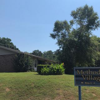 A building surrounded by trees with a sign on the lawn.