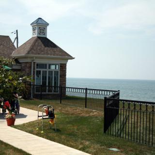 A coastal building with a view of the sea, surrounded by a fence and lawn where children are playing.