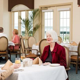 An elderly woman enjoying a meal and conversation at a restaurant.