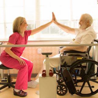 A physical therapist and a senior man in a wheelchair share a high-five during a rehabilitation session.