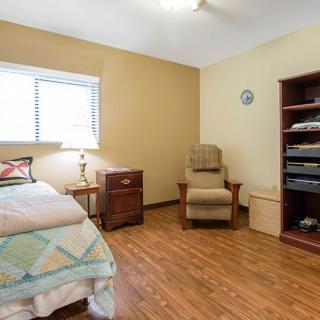 A cozy bedroom with a single bed, armchair, and wooden flooring.