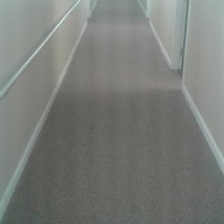 A view of a long, empty hallway with gray flooring and white walls.